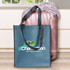 A denim tote bag with black handles and a logo, placed next to a pink suitcase and patterned fabric.