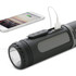 A black, cylindrical flashlight with a USB port for charging devices, alongside a smartphone connected to it.