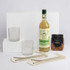 A green bottle of Margarita, two crystal glasses, a packet of pretzels, and metal straws on a white backdrop.