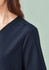 A close-up of a women's navy V-neck scrub top, featuring a slight shoulder detail and a branding logo.