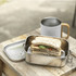A stainless steel lunch box with a sandwich inside, placed beside a drink bottle on a wooden surface.