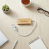 A bamboo USB hub with a white cable, placed on a wooden surface alongside a cup, notebook, and glasses.