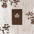 A brown A6 notebook surrounded by coffee beans on a wooden surface, featuring a logo on the cover.