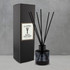 A round black reed diffuser with five black reeds, presented in a black box, featuring a label.