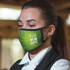 A green reusable face mask featuring a design with dots and a logo, worn by a woman in a formal shirt.