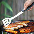 A BBQ multi tool with a silver spatula and a black handle, grilling various meats on a barbecue.