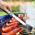 A BBQ multi-tool with a black handle and a silicone brush, applying marinade to grilled prawns and vegetables.
