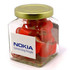 A glass jar filled with red rock candy pieces, featuring a gold lid and a branding sticker.