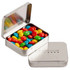 A rectangular, silver hinge tin filled with colourful chewy fruit sweets in red, blue, green, and yellow.