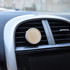 A car air freshener with a circular bamboo design, mounted on an air vent in a vehicle.