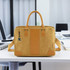 A yellow kraft paper satchel with tan accents and a logo, placed on a desk in an office setting.