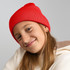 A red knitted beanie worn by a child with long hair, featuring a logo on the side.