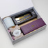 A gift box containing a cheese knife, caramel fudge, a candle, and a wooden board. The box is white with a logo.