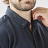 A close-up of a man's neck and collar in a dark navy short sleeve button-up shirt, featuring a logo.