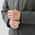 A close-up of a person's hands adjusting the cuffs of a dark grey thermal jacket with a logo.