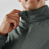A close-up of a man's hand adjusting the collar of a dark green thermal jacket, featuring a zipper and a logo.