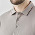 A men's long-sleeve polo shirt in a muted grey shade featuring a collar and button details. It includes a logo on the chest.