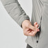 A hand adjusting the zipper of a light grey women's puffer jacket, featuring a sleek design and logo.