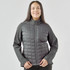A women's softshell jacket in grey with a quilted front and long sleeves. Features a zip-up front and a logo.
