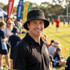 A man wearing a black Leroy Cord Bucket Hat smiles at a sports field, with people and tents in the background.