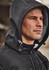 A man wearing a black unisex softshell jacket with a hood, featuring a branded logo on the chest.