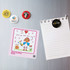 A collection of colourful button badges, including a drawing, displayed on a metallic surface with a notepad.