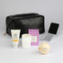A black toiletry bag containing a tube of cream, a candle, a mirror, a bath bomb, and a boxed product.