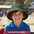 A green bucket hat on a smiling child, with a playground scene in the background. The hat has a logo.