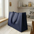 A large navy blue non-woven shopper bag with sturdy handles rests on a kitchen counter. It features a subtle branding logo.