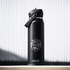 A drink bottle in matte black with a flip straw lid and a logo featuring a vanlife theme.