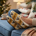 Custom knitted slippers in yellow, black, and cream, featuring a festive pattern, placed on a blue couch beside decorative pillows.