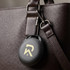 A black Bluetooth tracker attached to a brown leather bag, featuring a minimalist logo on its surface.