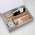 A gift box containing a bottle of sparkling wine, a wooden chopping board, and caramel fudge. The box has a minimalist design.