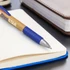 A bamboo pen with a blue grip resting on an open notebook beside a brown leather journal.