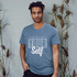 A unisex T-shirt in a soft blue colour featuring a large motivational phrase. The shirt has a logo on it.