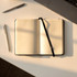 A black bound journal with lined pages, resting on a desk beside a pen and a laptop.
