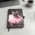 A notebook with a black cover featuring a pink tutu-wearing dog on the front. It includes a logo.
