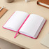 A pink bound journal with lined pages, lying open on a desk surface.