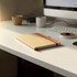 A brown journal with a red elastic band rests on a minimalist desk, accompanied by a cup and electronic devices.