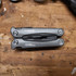 A grey multi-tool with multiple functions, featuring a sleek design and a logo, resting on a wooden surface.