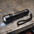 A black torch with a textured grip and a wrist strap, featuring a bright LED light at the front.