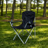 An oversized folding chair in black with silver accents, set on green grass in a wooded area.