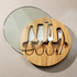 A round bamboo cheese board set featuring four stainless steel knives and a corkscrew, with a glass lid.