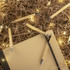 A collection of bamboo pens in natural colour scattered around a notebook and decorative lights on brown filler material.