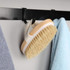 A wooden body brush with a beige bristle head and a white base, hanging on a hook beside towels.