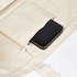 A large cream canvas tote bag with a black smartphone tucked into a zippered pocket.