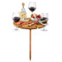 A wooden outdoor party table with a stake, holding wine glasses, cheese, strawberries, and utensils.