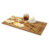 A wooden cheeseboard features a selection of cheeses, crackers, nuts, and a jar of jam, with gold knives included.