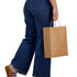 A person in blue jeans holds a large brown paper bag with handles, standing in a casual pose.