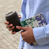 A reusable coffee cup in dark brown held with a patterned notebook. The person is wearing a light blue shirt.